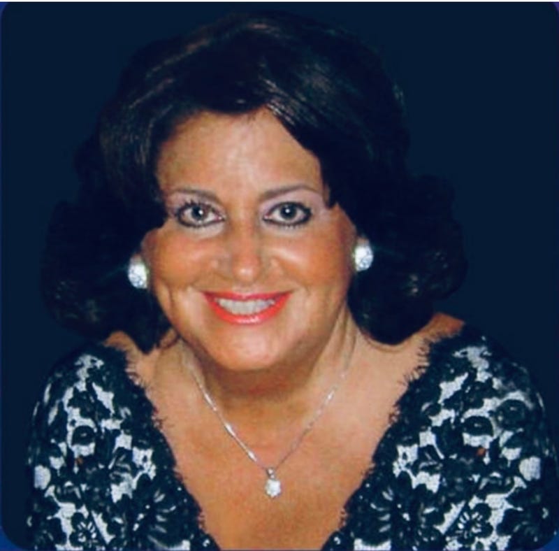 Photo of older woman with tan skin, makeup and jewelry in black lace dress smiling 