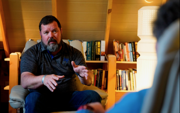 Reg McCutcheon sits in a chair and speaks to someone