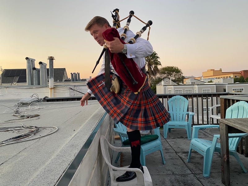 Wilkes ascends his roof to play his bagpipes for his neighbors at sunset.