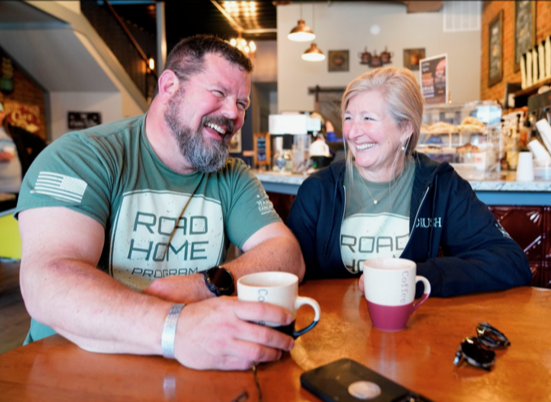 Reg McCutcheon sits in a coffee shop with a woman, both of them laughing.