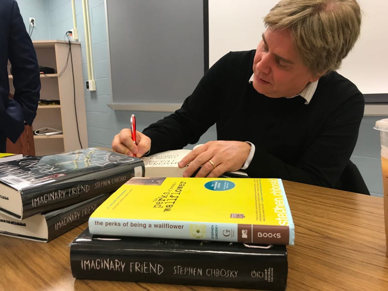 Author Stephen Chbosky signs a book while sitting at a desk