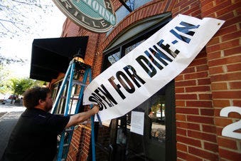 FILE - In this April 27, 2020, file photo, Jason Godbey hangs a banner over the entrance of Madison Chop House Grille as they prepare to shift from take out only to dine-in service in Madison, Ga. (AP Photo/John Bazemore, File)