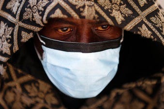 A man wears a protective mask while waiting for a bus in Detroit, Wednesday, April 8, 2020. (AP Photo/Paul Sancya)
