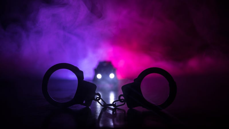 Closed handcuffs on the street pavement at night with police car lights - stock photo