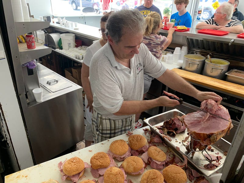 Photo of Harry Lile, Owner of Lile's Ham Shop, cutting ham during the closing day of the community staple restaurant