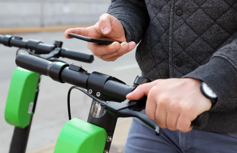 A person holds a phone in his hand while he prepares to ride an electric scooter.