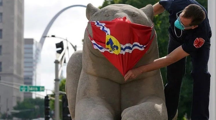 A man puts a St. Louis-flag mask over a statue in the city.