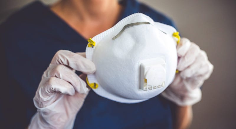 a medical worker wearing gloves holds an N95 style facemask