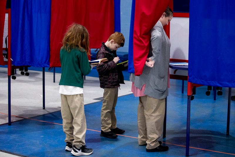 Samantha Murch accompanied by her two boys Alexander, 8, center, and Jacob, 11, left, votes in the New Hampshire primary at Bishop O'Neill Youth Center, Tuesday, Feb. 11, 2020, in Manchester, N.H. (AP Photo/Andrew Harnik)