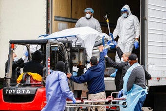 A body wrapped in plastic is unloaded from a refrigerated truck and handled by medical workers wearing personal protective equipment due to COVID-19 concerns. (AP Photo/John Minchillo)