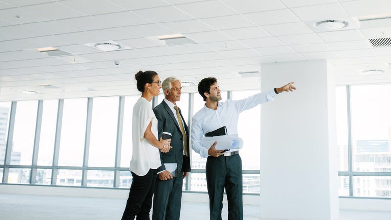 Real estate broker showing office space to clients. Business people and real estate agent at empty office space, with estate broker pointing at something interesting.