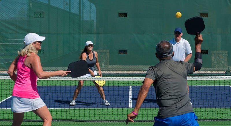 four people play pickleball, a game like tennis with a wiffle ball