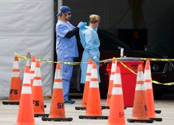 FILE - In this July 5, 2020, file photo, healthcare workers help each other with their personal protective equipment at a drive-thru coronavirus testing site outside Hard Rock Stadium in Miami Gardens, Fla. (AP Photo/Wilfredo Lee, File)