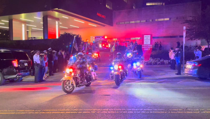 A procession of police officers at Penn Presbyterian Medical Center escort an ambulance carrying the Philadelphia police officer who was shot and killed in an airport parking garage on Oct. 12, 2023.