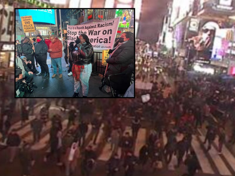 Foreground: A protester speaks to the crowd at Times Square. Background: protesters march south out of Times Square toward Union Square.
