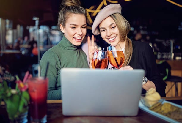 Two Ladies Toasting Cocktails At A Laptop