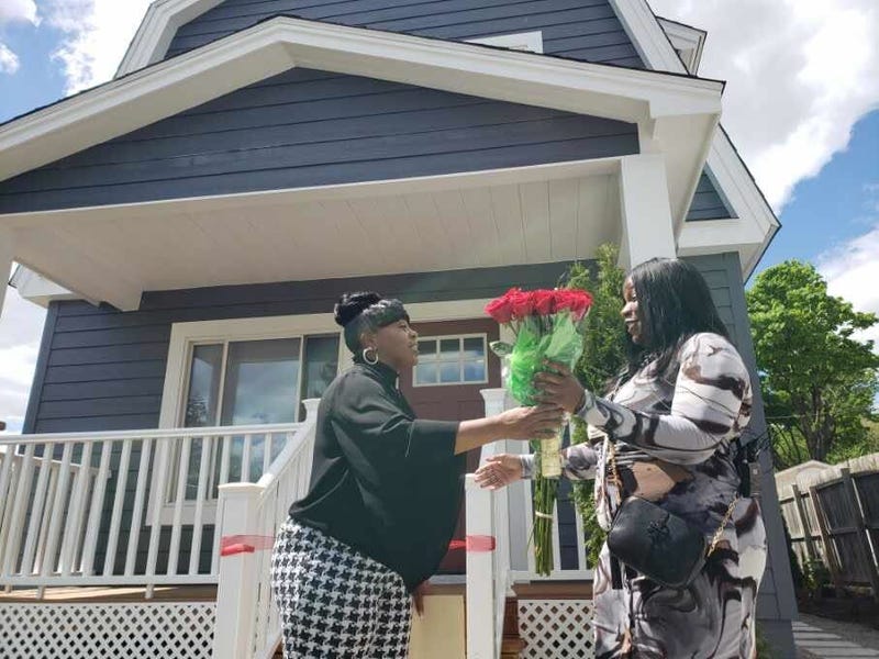 Woman receiving flowers in front of home from another woman