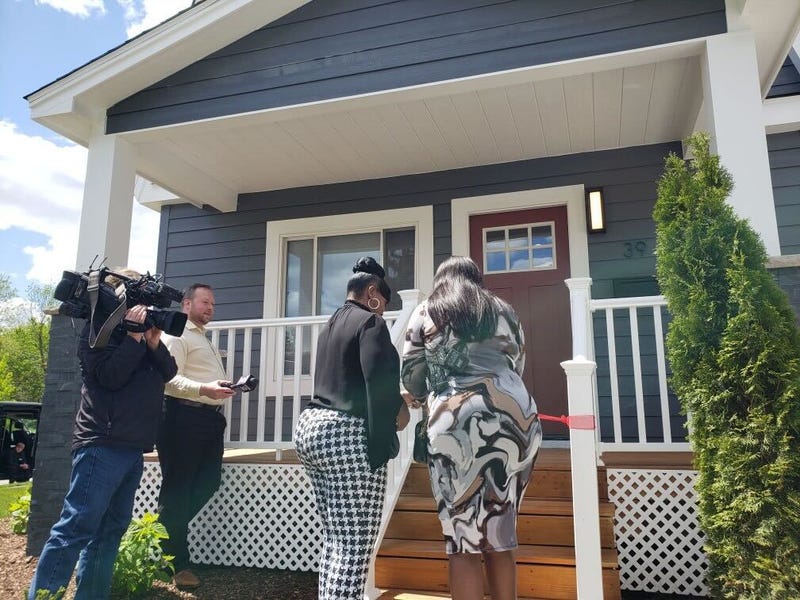 Two women walking into home, with camera man and reporter on side