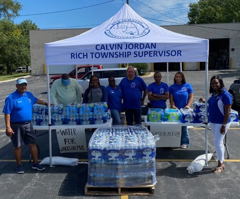 Several people stand under a tent as they accept water donations