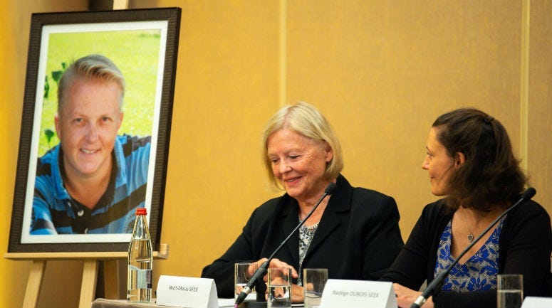 Nadege Dubois-Seex (right) at a Paris press conference on May 21 alongside a portrait of her late husband, Jonathan Seex, and his mother Britt-Marie Seex (center).