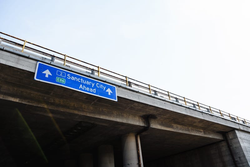 A blue traffic road sign with the message "Sanctuary City Ahead"