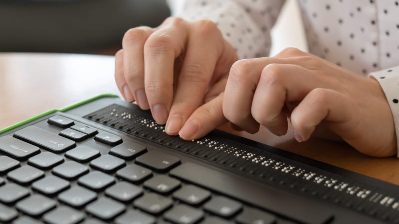 A blind woman uses a computer with a Braille display and a computer keyboard