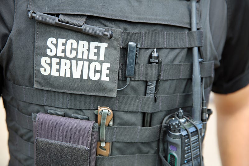 U.S. Secret Service officer, wearing a vest with various equipment attached, stands in front of White House