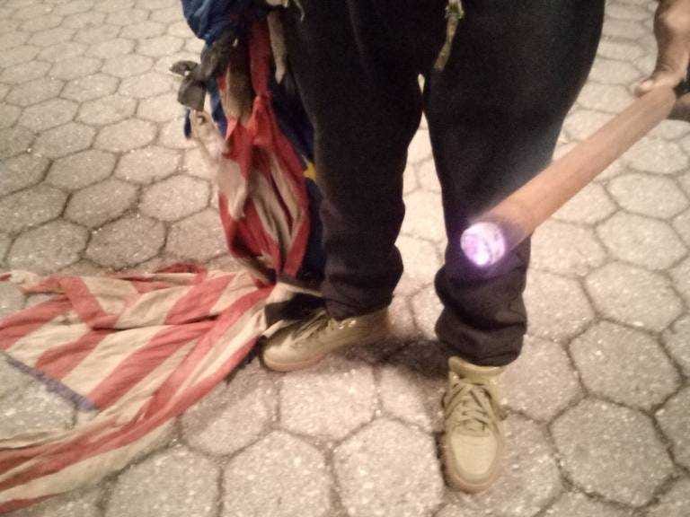 A protester at Union Square holds a lit incense stick and a tattered American flag.