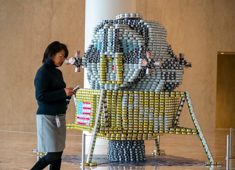 Woman walking by a sculpture of a spaceship made from cans of food