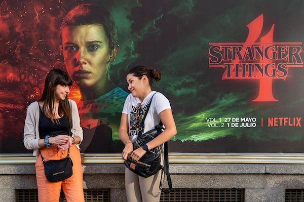 Women talk in front of a street commercial advertisement banner from the American global on-demand Internet streaming media provider Netflix featuring Stranger Things Season 4 TV show in Spain
