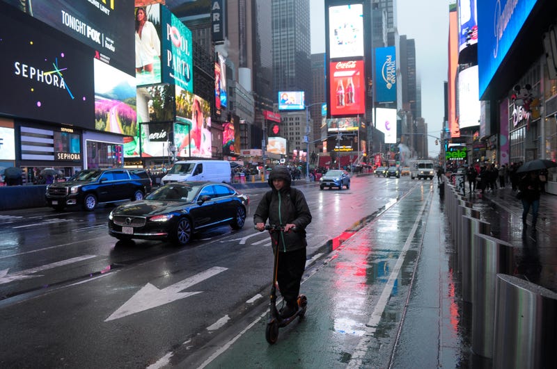 A person rides an electric scooter through Times Square, New York City on a rainy day