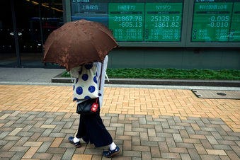 A woman walks past an electronic stock board showing Japan's Nikkei 225 index and New York Dow index at a securities firm in Tokyo Friday, June 12, 2020. (AP Photo/Eugene Hoshiko)