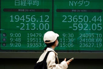 A woman wearing a mask against the spread of the new coronavirus walks past an electronic stock board showing Japan's Nikkei 225 and New York Dow index at a securities firm in Tokyo Tuesday, April 21, 2020. (AP Photo/Eugene Hoshiko)
