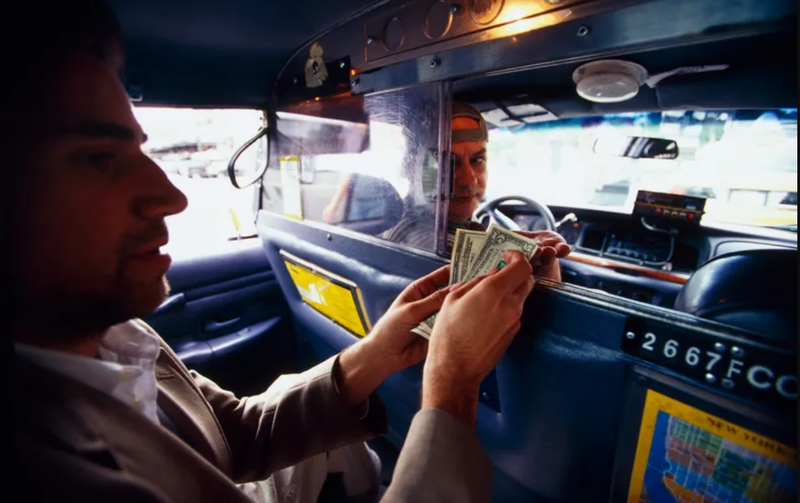 A man hands cash to a taxi driver.
