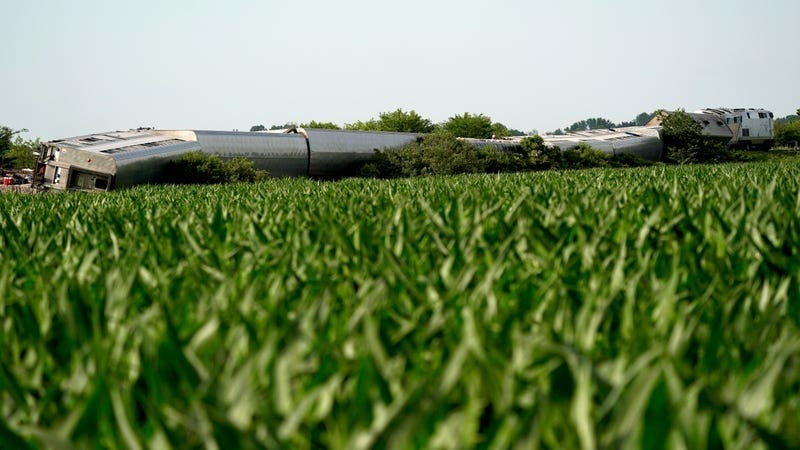 The Amtrak train on its side, seen beyond a corn field