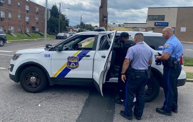 Two Philadelphia police officers place suspect Rasheem Trusty into a squad vehicle.