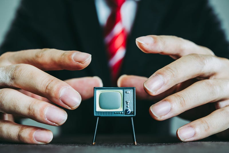 A small television with a businessman in background