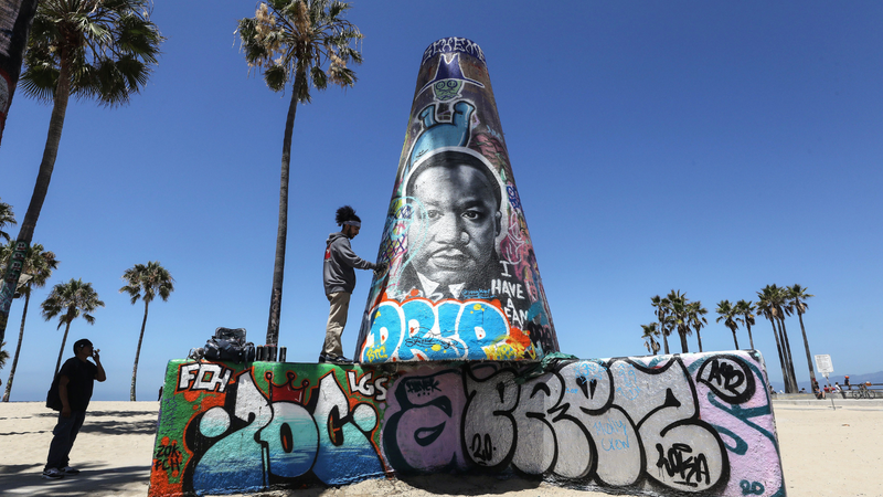 An artist paints graffiti near an image of Dr. Martin Luther King Jr. at the closed and mostly empty Venice Beach