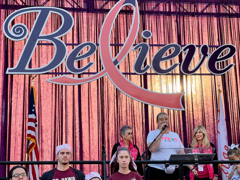 Pepper on stage at the Believe Walk 2024, flanked by founders Cathy Stockton and Annie Sellas