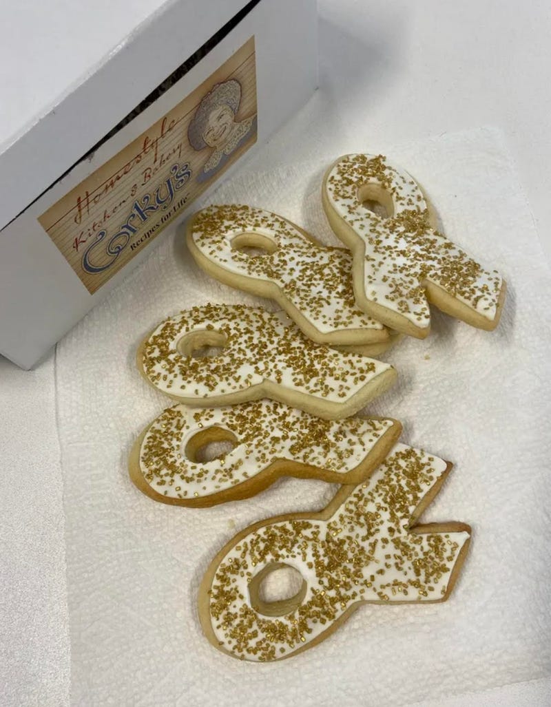 A half dozen sugar cookies shaped like a ribbon with gold sprinkles