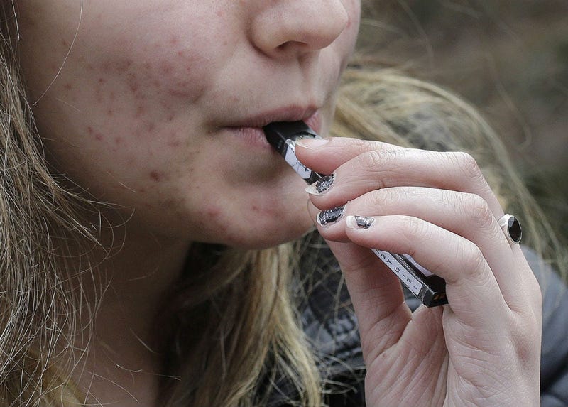 In this April 11, 2018 file photo, a high school student uses a vaping device near a school campus in Cambridge, Mass.