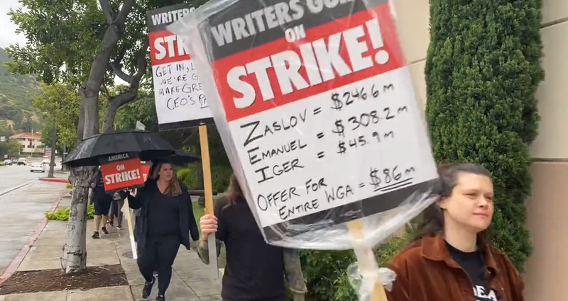 picketer with sign that says zaslov = $246.6m emanuel = $308.2m iger = $45.9m offer for entire wga = $86m"