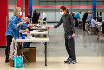 Bridget McDonald, right, receives a ballot from poll worker Patty Piek-Groth on Tuesday, April 7, 2020, at the Janesville Mall in Janesville, Wis. (Angela Major/The Janesville Gazette via AP)